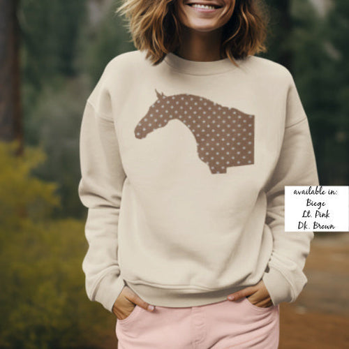 Woman wearing a beige sweatshirt with a horse design, standing outdoors.